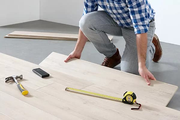 Vloerlegger legt lichte planken in houtlook, met hamer en rolmaat