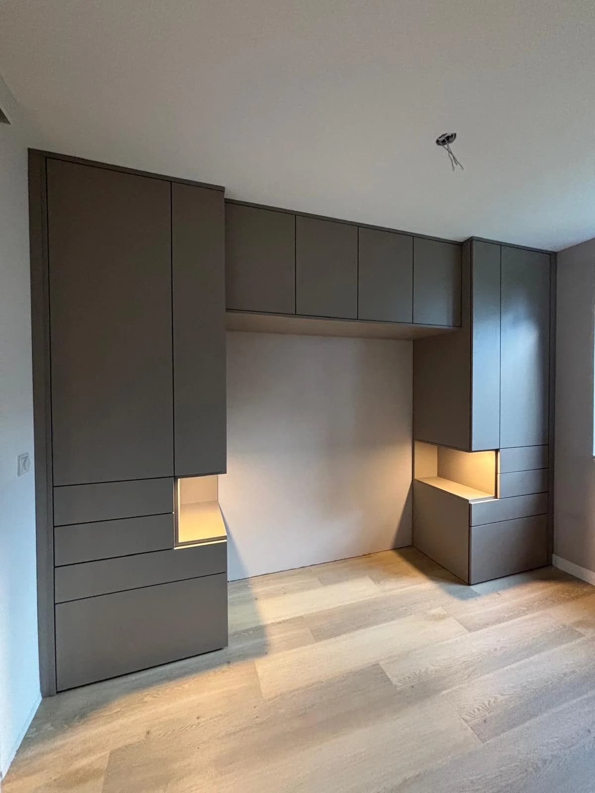 Taupe kastenwand rond het bed met verlichte nissen