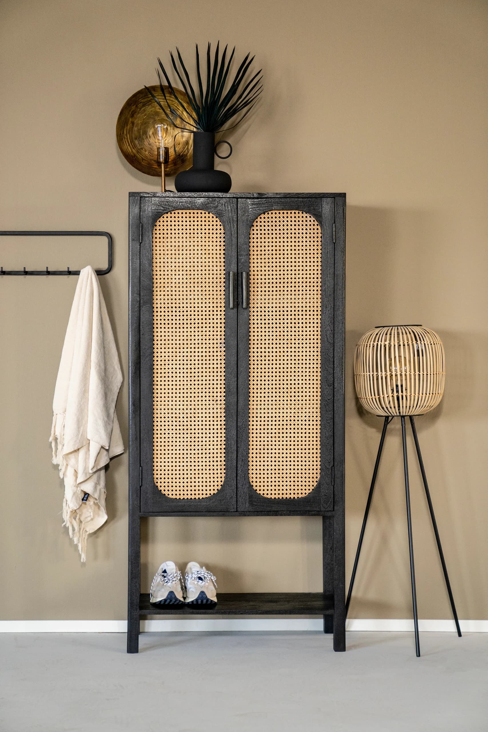 Zwarte kast met rotan deurtjes, kapstok en vloerlamp in de hal