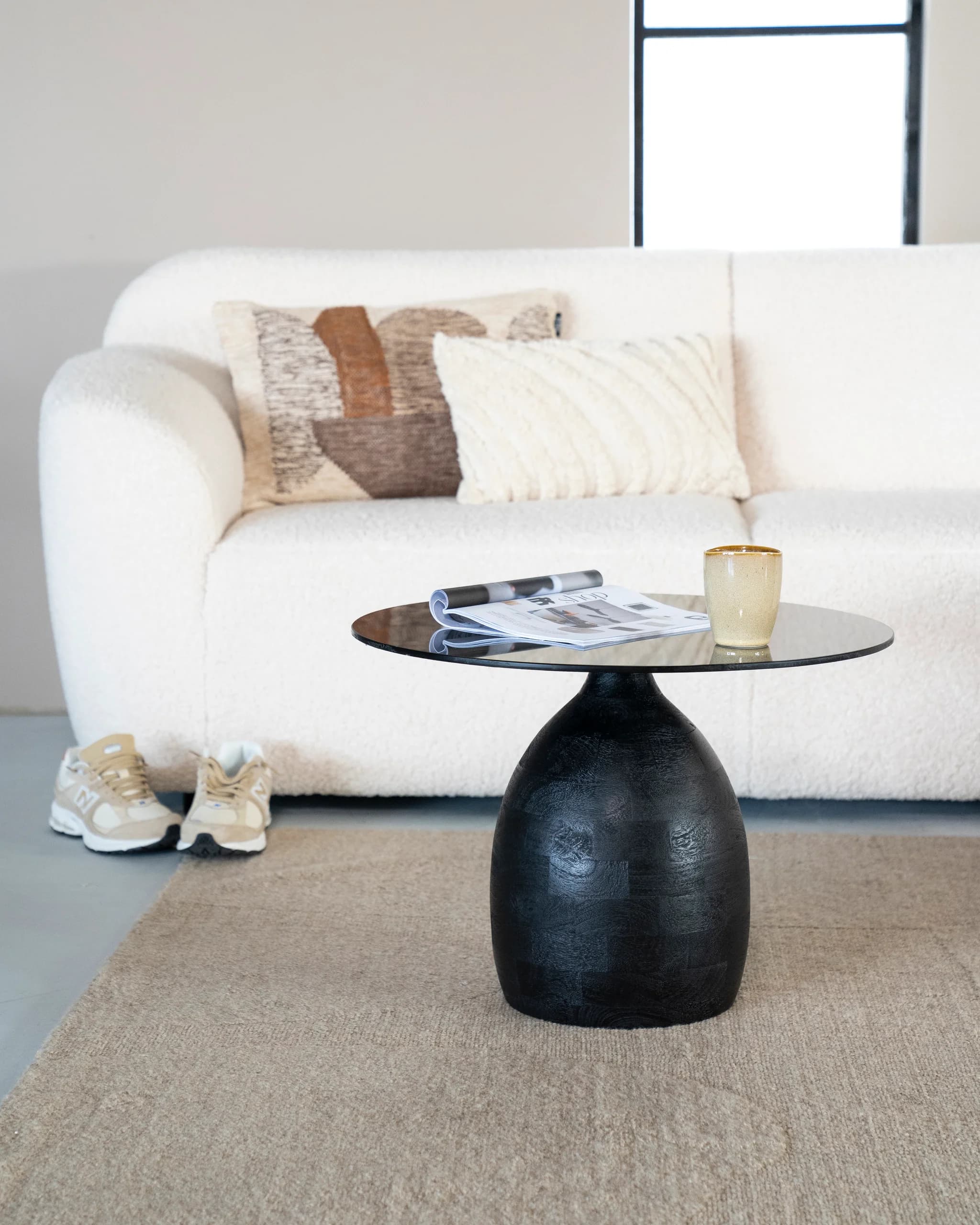 Ronde salontafel met zwarte voet en glazen blad voor een witte bouclébank