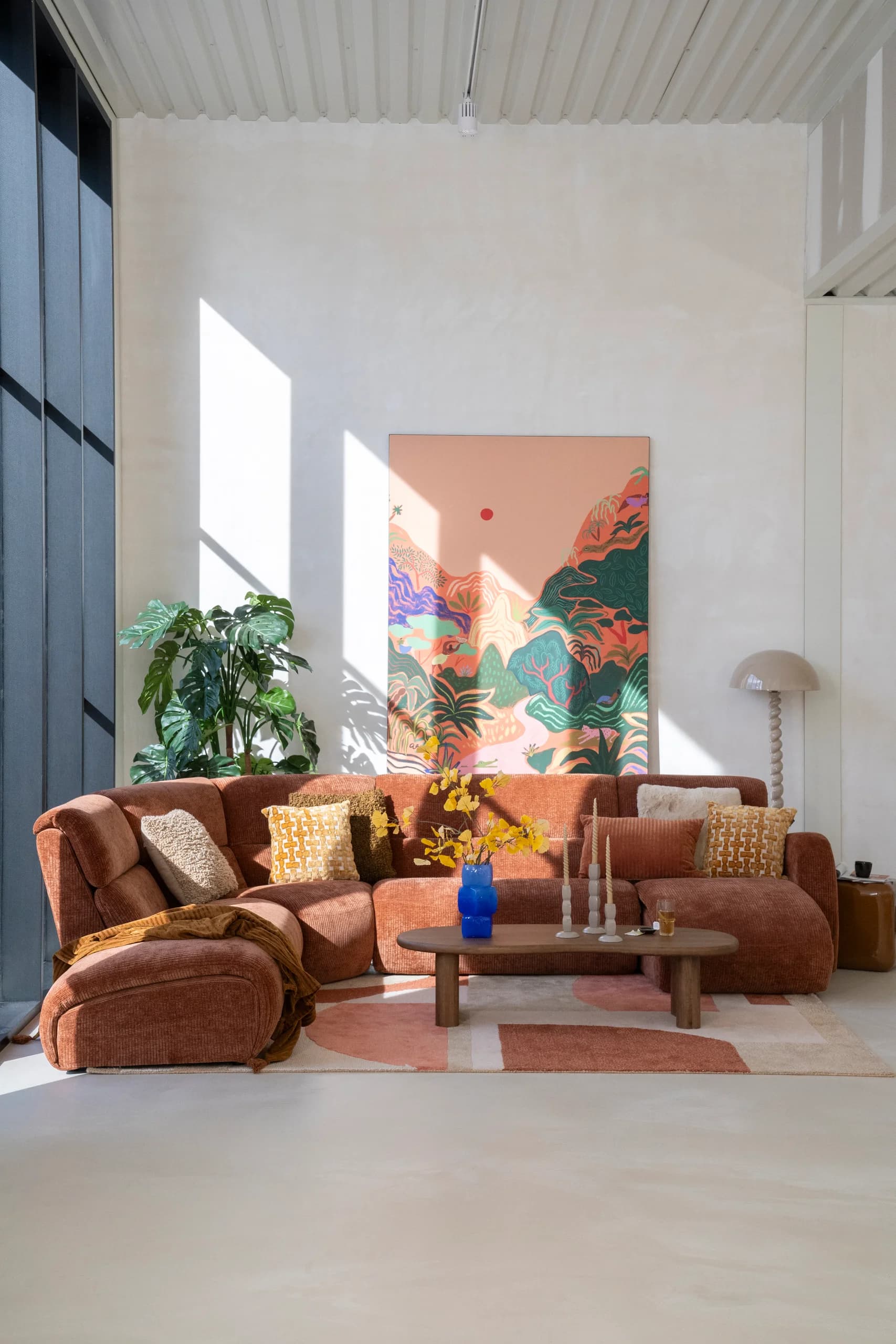 Hoge loftwoonkamer met terracotta hoekbank, kunst en planten